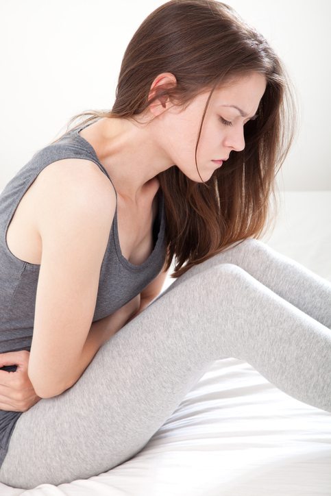 Young woman in gray clutching her stomach in pain