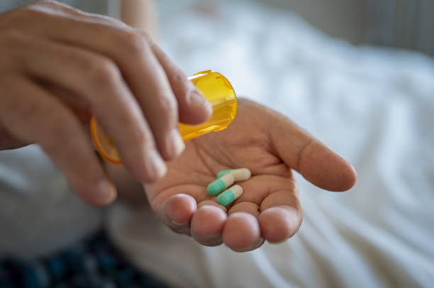 Image of an antimicrobial sitting on a table. Closeup of woman hand pouring capsules from a pill bottle into hand. Senior woman taking daily medicine to consume. Close up of male hands taking daily dose of drug.