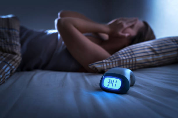 Image of a dietitian holding a stack of papers in hand which are test results. Sleepless woman suffering from insomnia, sleep apnea or stress. Tired and exhausted lady. Headache or migraine. Awake in the middle of the night. Frustrated person with problem. Alarm clock with time.