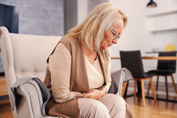 photo of large intestine is on the senior woman body against gray background, People With Stomach ache problem concept, Female anatomy ick senior woman sitting at home in her chair and holding her stomach. She is in pain.