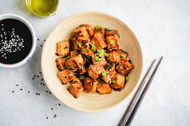 Image of a dietitian holding a stack of papers in hand which are test results. Stir fried marinated tofu with sesame seeds, soy sauce and scallions in a bowl, top view