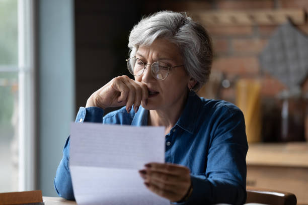 Image of a dietitian holding a stack of papers in hand which are test results. Ugly news. Distressed old age female opened letter from hospital about her diagnosis.