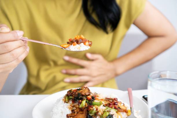 Person with fodmap intolerance eating food and having IBS flare or heartburn hand holding a spoon with chili peppers another hand holding her stomach ache