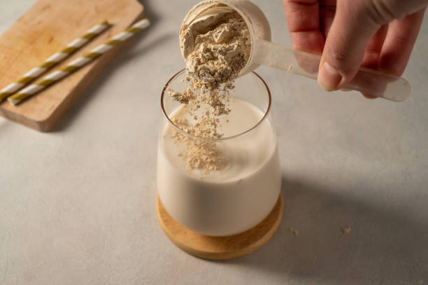 Image of an antimicrobial sitting on a table. Pouring protein powder from scoop, in glass with milkshake