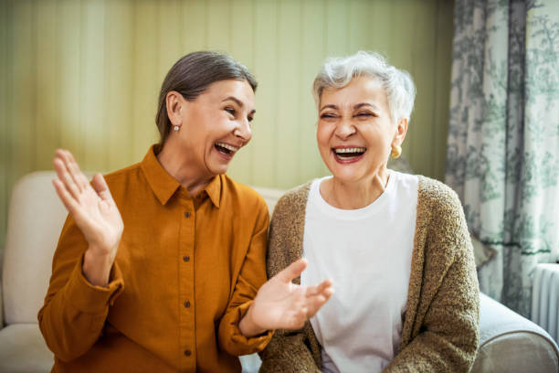 Image of an antimicrobial sitting on a table. Elderly sisters watching comedy together indoors, laughing. Portrait of two beautiful Caucasian women relaxing at home, sitting on sofa, opening mouth wide opened, enjoying weekend, having fun.