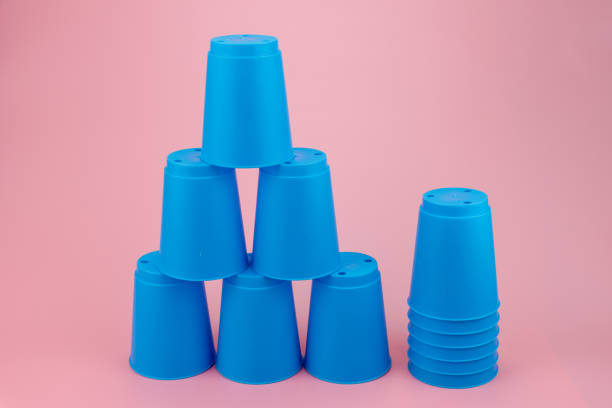 Image of a dietitian holding a stack of papers in hand which are test results. blue stacks plastic cups. Speed stack cup on pink background